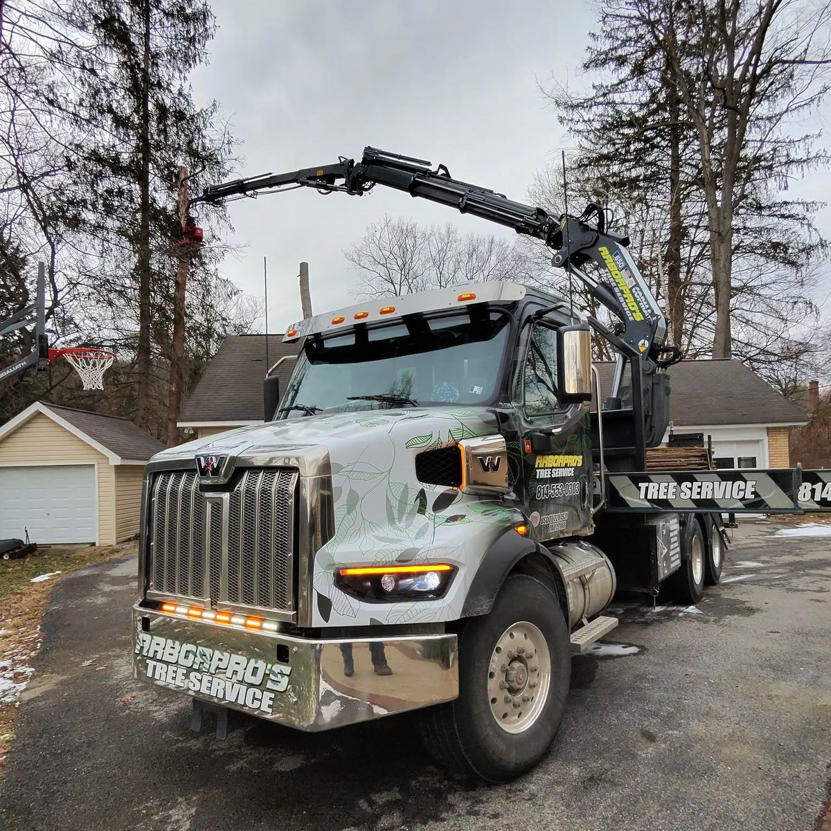 Arbor Pro’s crane truck in a winter driveway with the boom raised